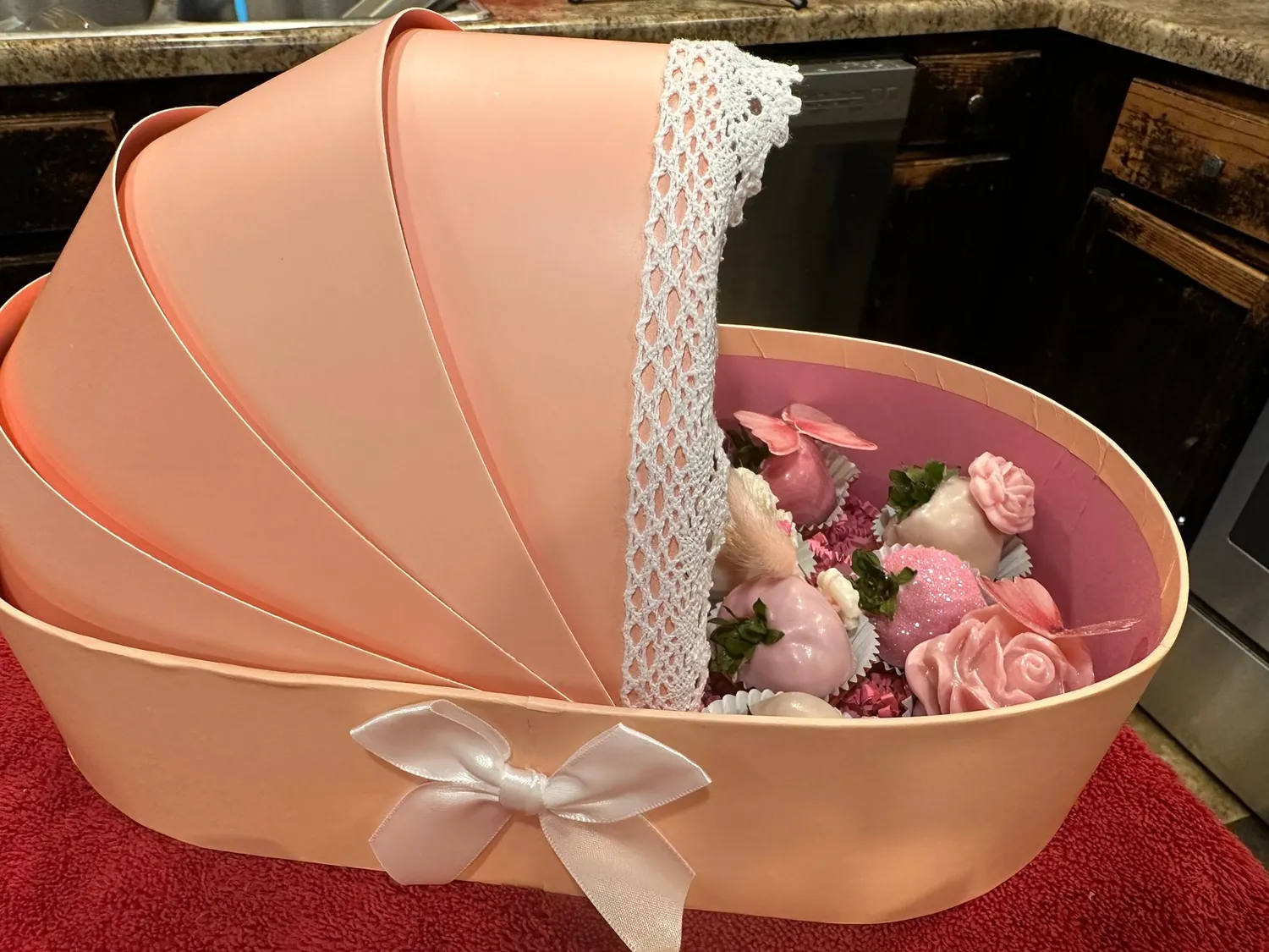 Peach baby-carriage box with a lace hood, filled with pink chocolate-covered strawberries
